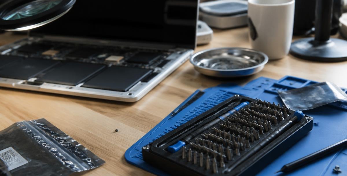 Repair bench with a disassembled laptop, precision bit set and anti-static mat